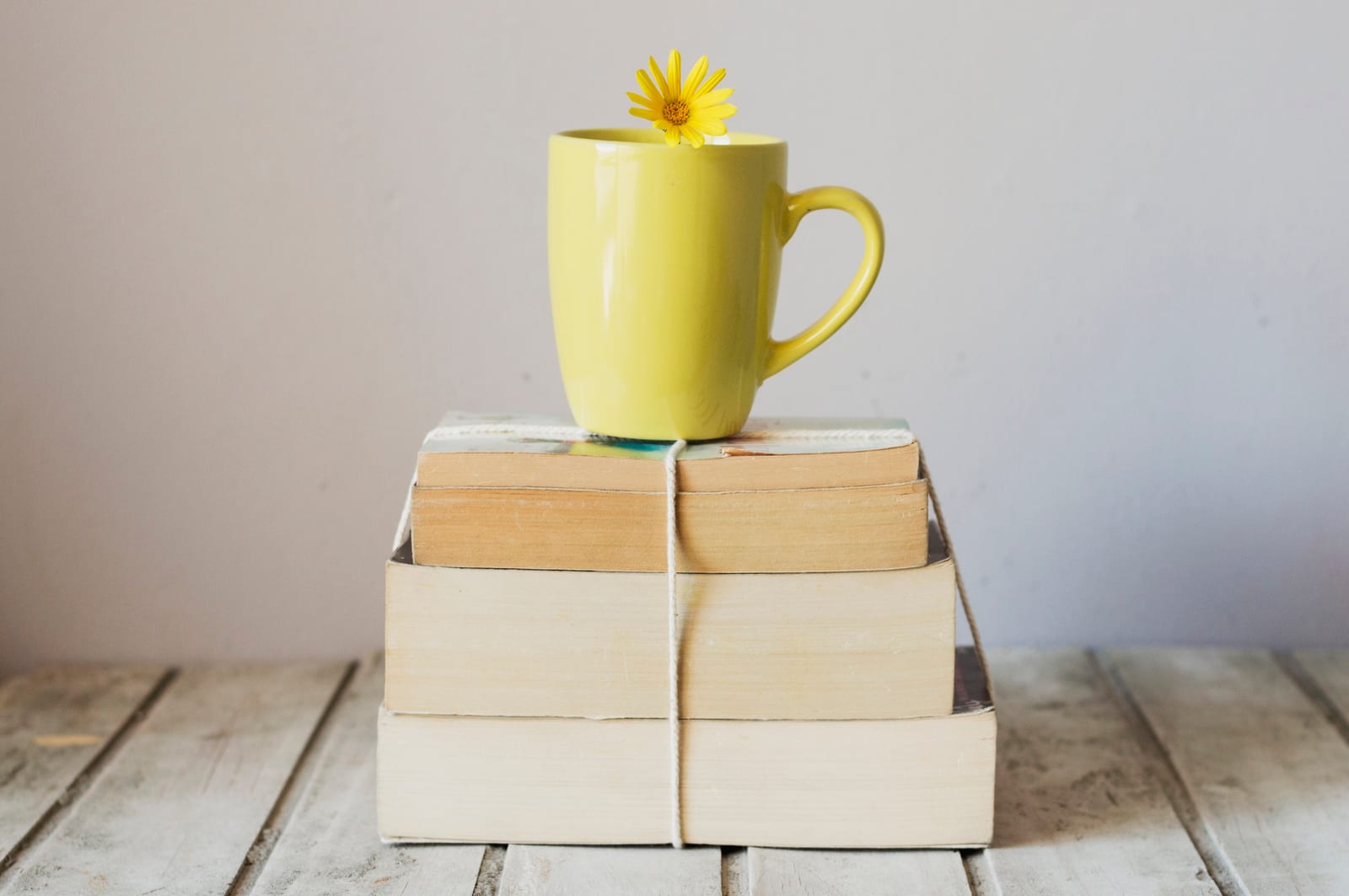 Uma caneca amarela com uma flor sobre uma pilha de livros amarrada com barbante.