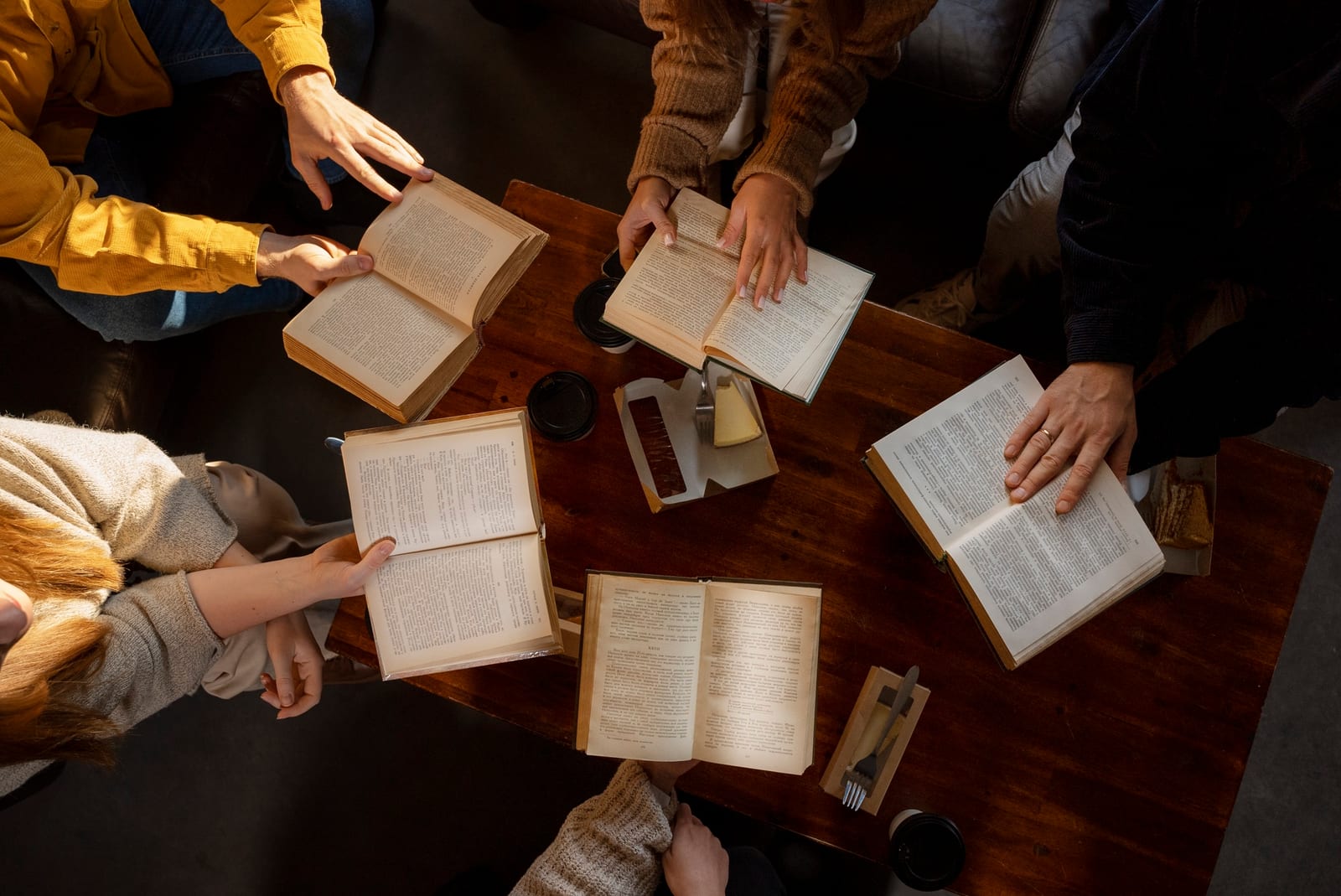 Várias pessoas sentadas ao redor de uma mesa, cada uma segurando um livro aberto, em um encontro de leitura.
