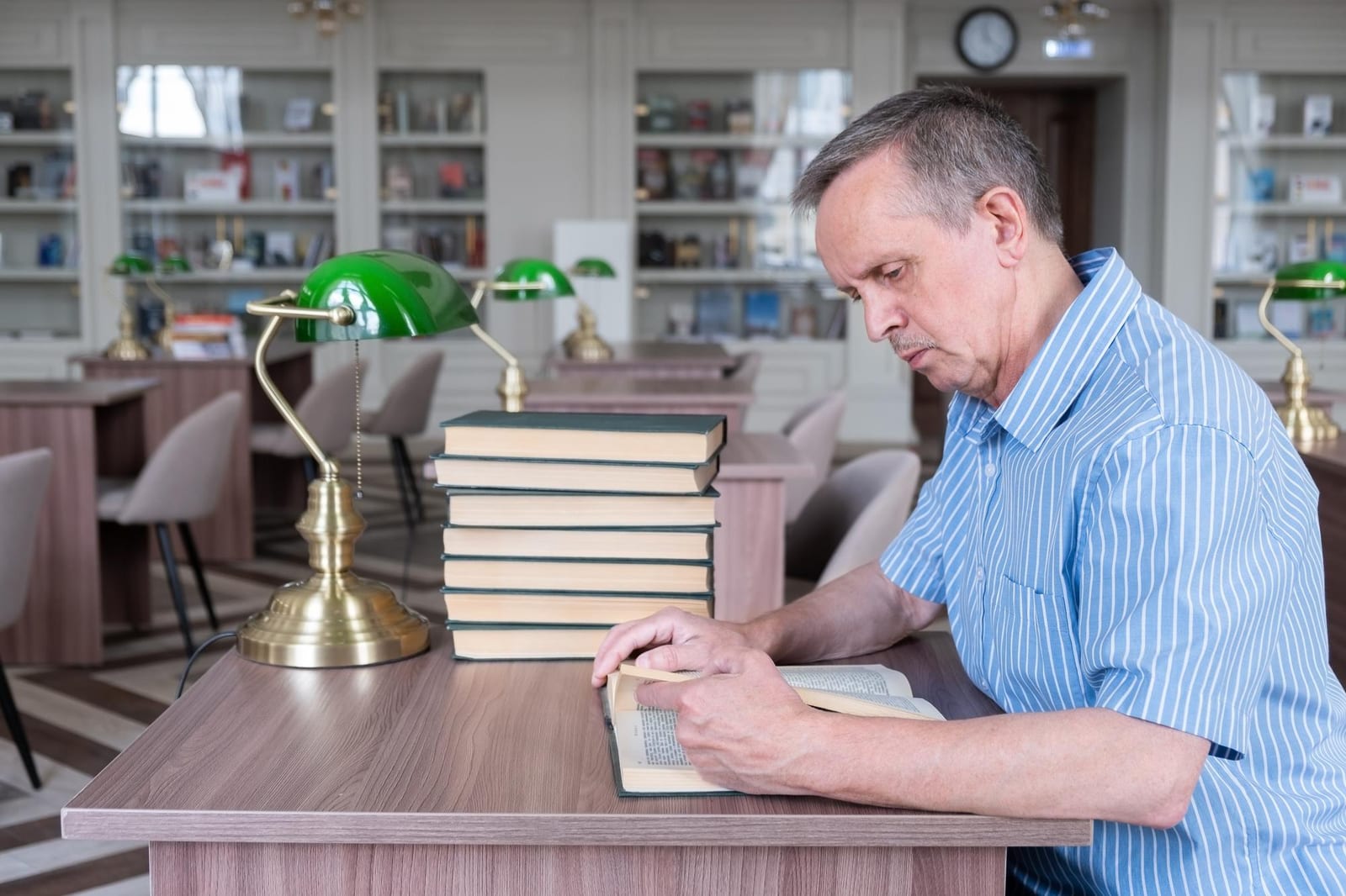 Um leitor concentrado em uma biblioteca, folheando um livro sobre uma mesa de madeira ao lado de uma pilha de volumes.